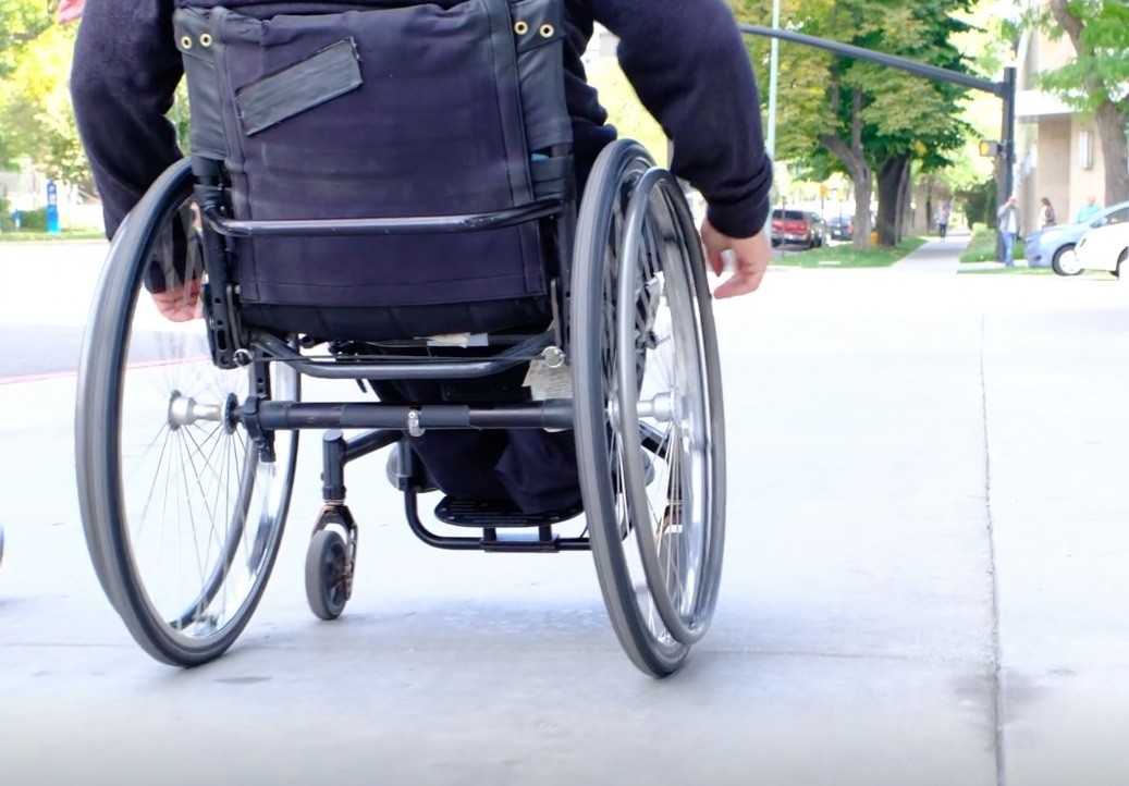 Adult male in black coat and black pants rolling himself away from the camera in a manual wheelchair