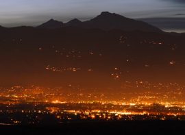 nighttime distance shot of the lights of boulder with sunset behind the mountains in the background