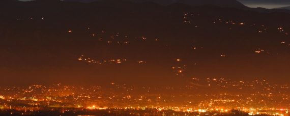 nighttime distance shot of the lights of boulder with sunset behind the mountains in the background