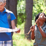 two multiracial youth looking at a map. two younger multiracial children playing with sticks