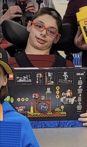 male youth holding a lego set in front of him smiling at the camera